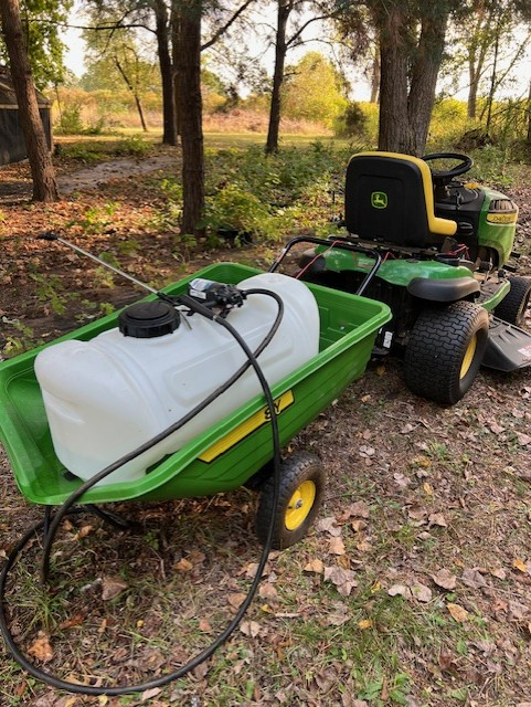 A white plastic water tank transported in a green lawn cart towed by a green tractor.